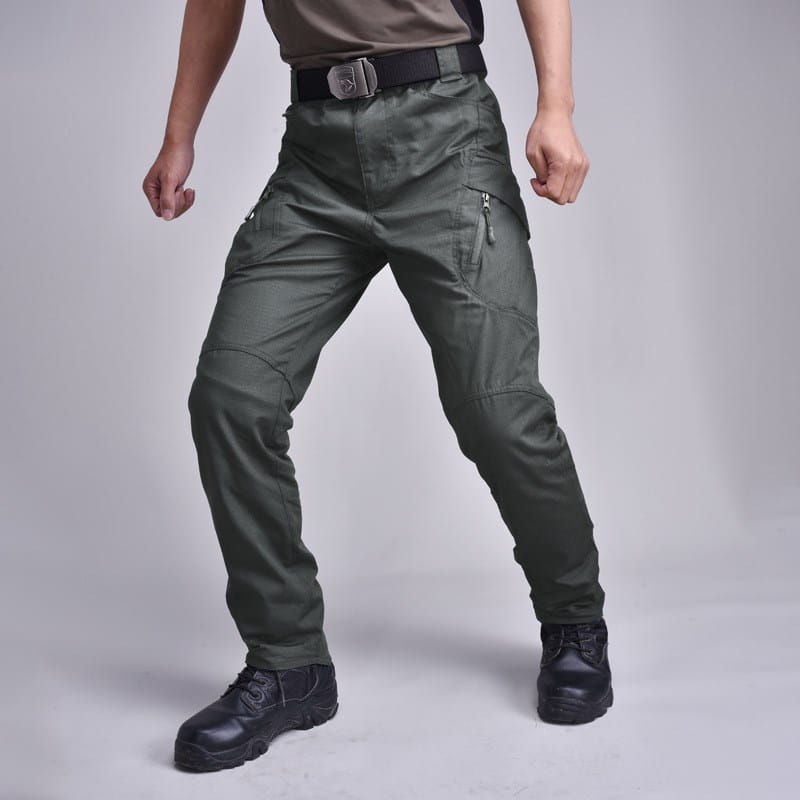 Dark olive green tactical military combat pants for men featuring multiple zippered pockets and reinforced knee areas.