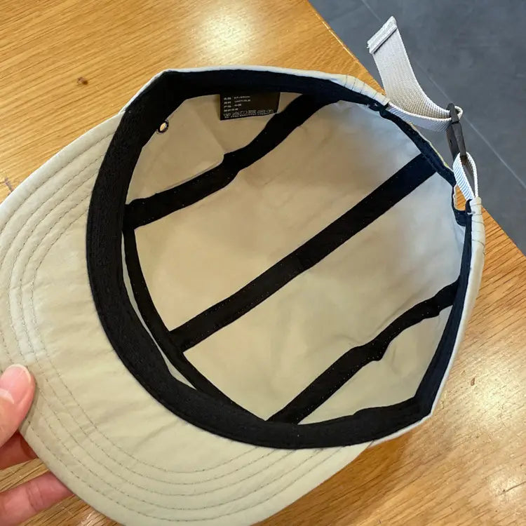 Beige quick drying five-panel cap with black inner lining and adjustable strap shown from the back side.