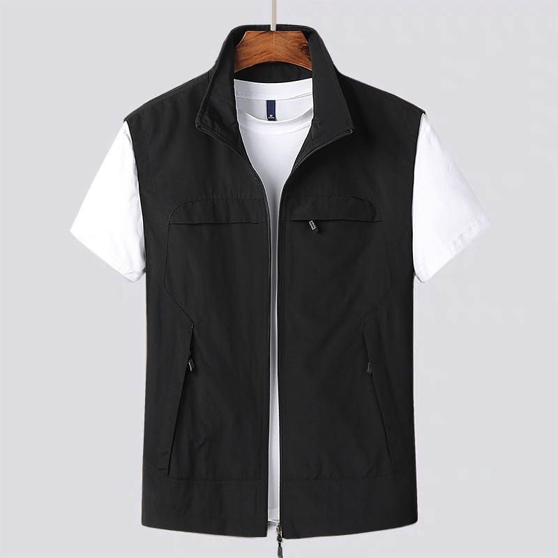 Chaleco utilitario impermeable negro con múltiples bolsillos, con cremallera frontal y tres bolsillos que se llevan sobre una camisa blanca de manga corta.