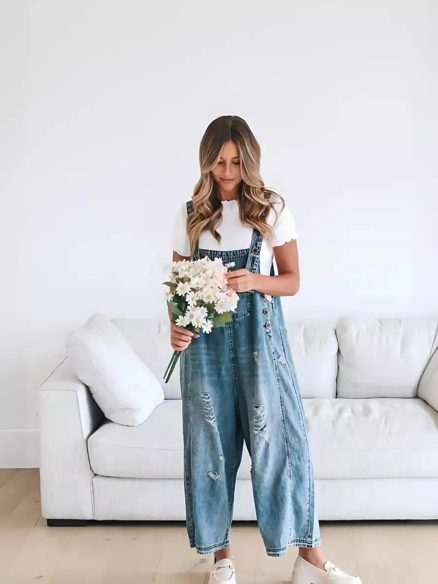 Women’s distressed denim overalls in light wash with a relaxed distressed fit and button closures featuring adjustable straps.