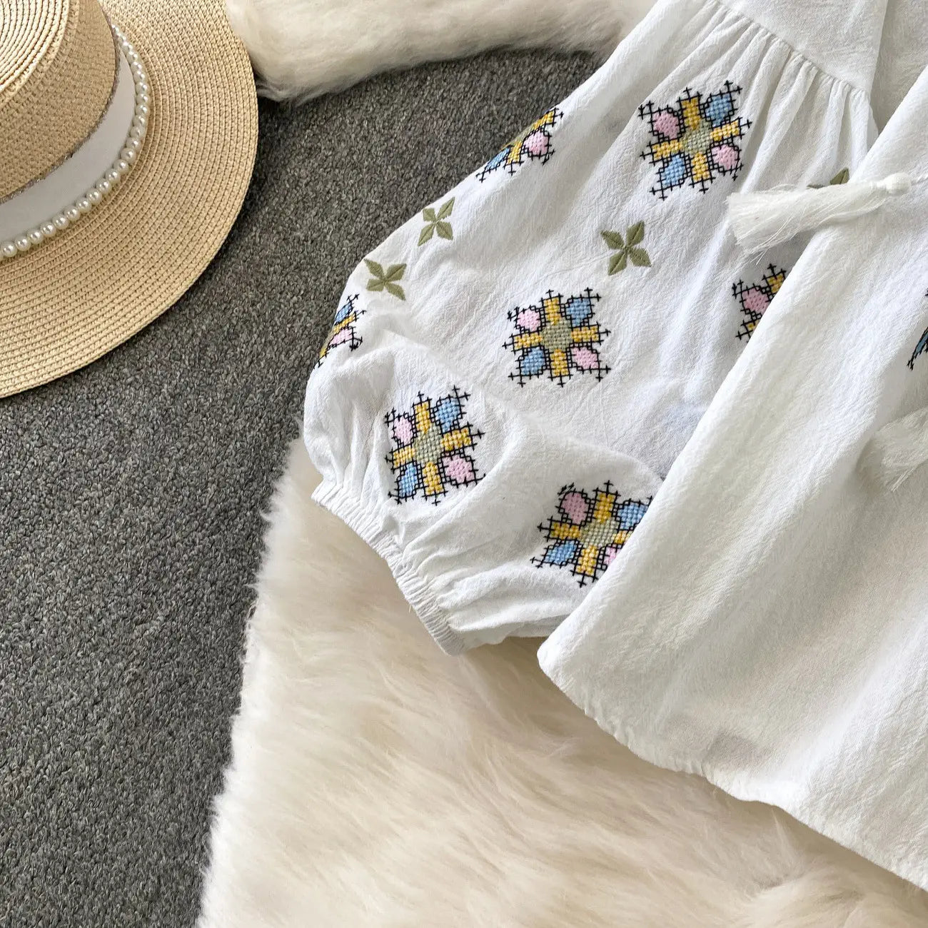 White embroidered lantern sleeve tie neck blouse featuring colorful cross-stitch embroidery in pastel blue pink and yellow on soft cotton fabric.