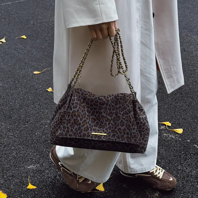 A brown leopard print crossbody bag made of leather with a gold tone chain strap for stylish wear.