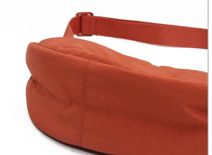 A soft rust-orange nylon dumpling messenger bag with a padded rounded body and curved adjustable crossbody strap.