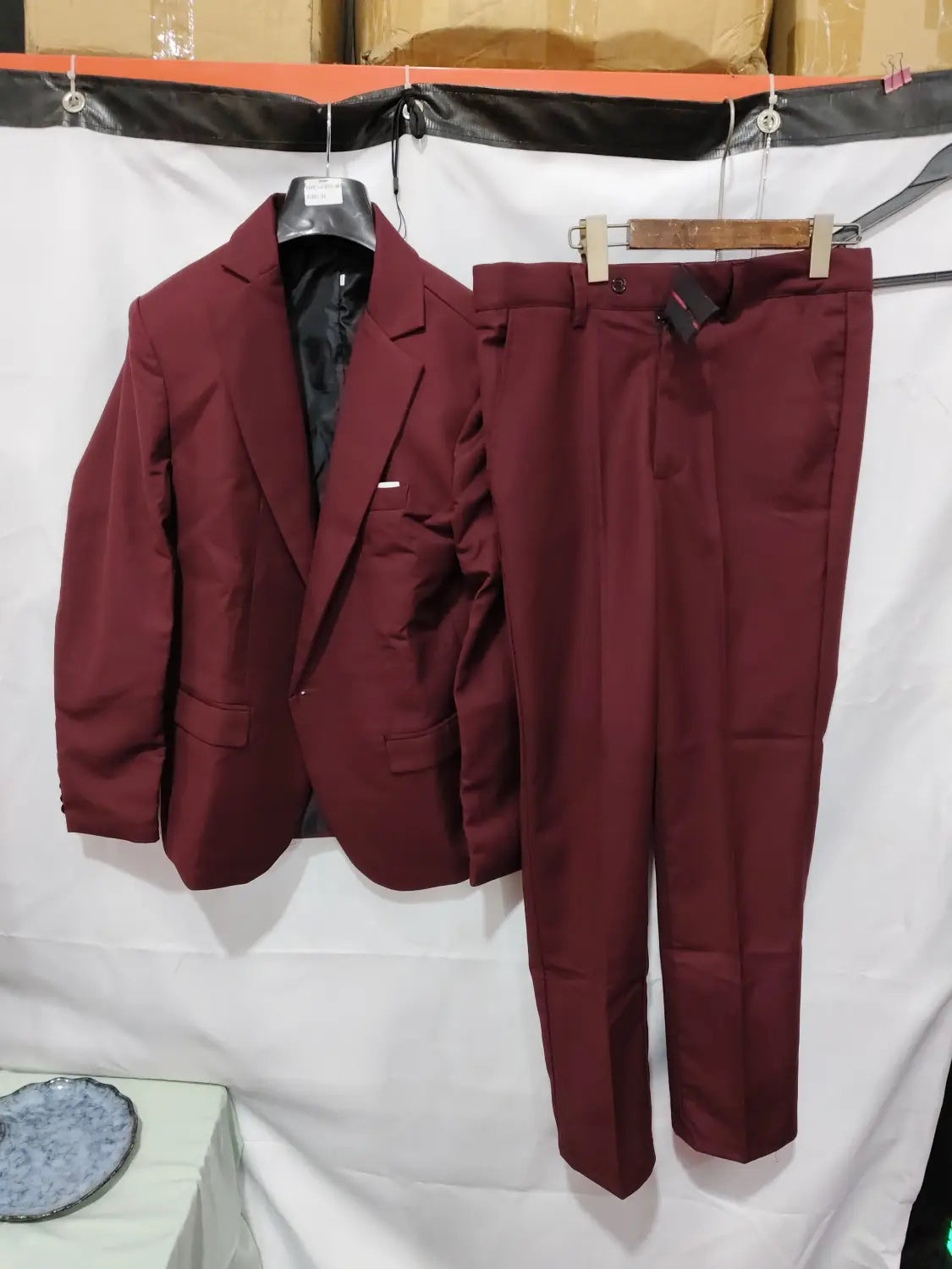 A men slim fit satin suit two piece consisting of a maroon tailored blazer and matching trousers made of smooth fabric with subtle creases.