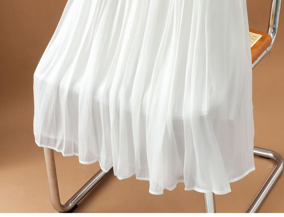 Ein fließender weißer irrisierender Chiffon-Faltenrock aus leichtem, halbtransparentem Material, der sich elegant über einen modernen Stuhl drapiert.