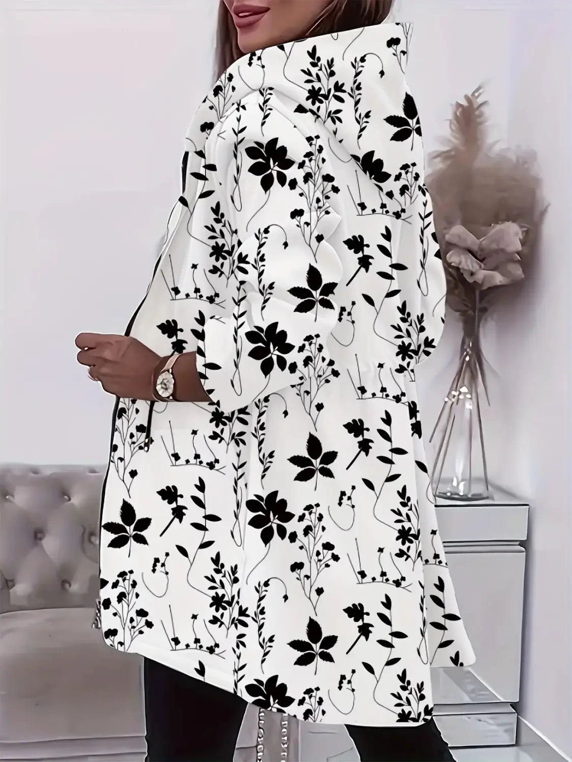 Veste à capuche zippée blanche, avec une fermeture éclair, présentant un motif floral brodé noir sur un fond blanc.