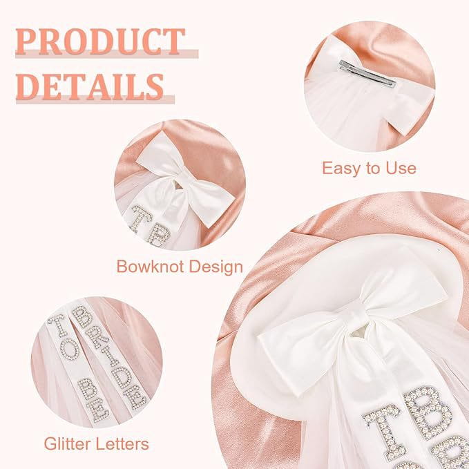 A delicate pink satin bridal bow veil baby bonnet featuring a prominent white bowknot and sparkling rhinestone bride to be lettering tbd on the front.