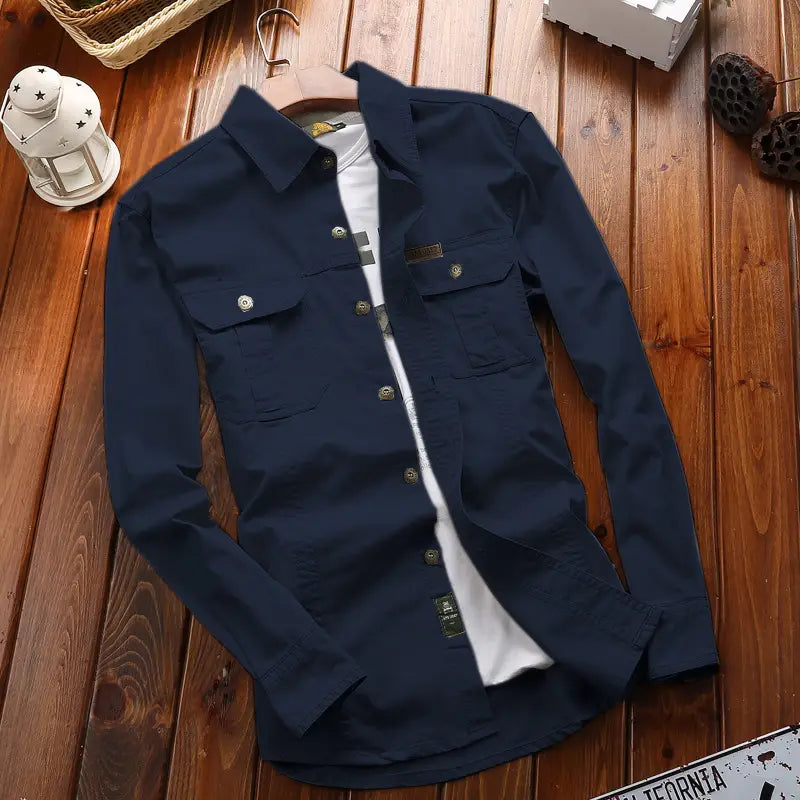 Chemise d’homme d’extérieur à manches longues boutonnée unie bleu marine foncé, avec deux poches de poitrine, portée par-dessus un t-shirt blanc.