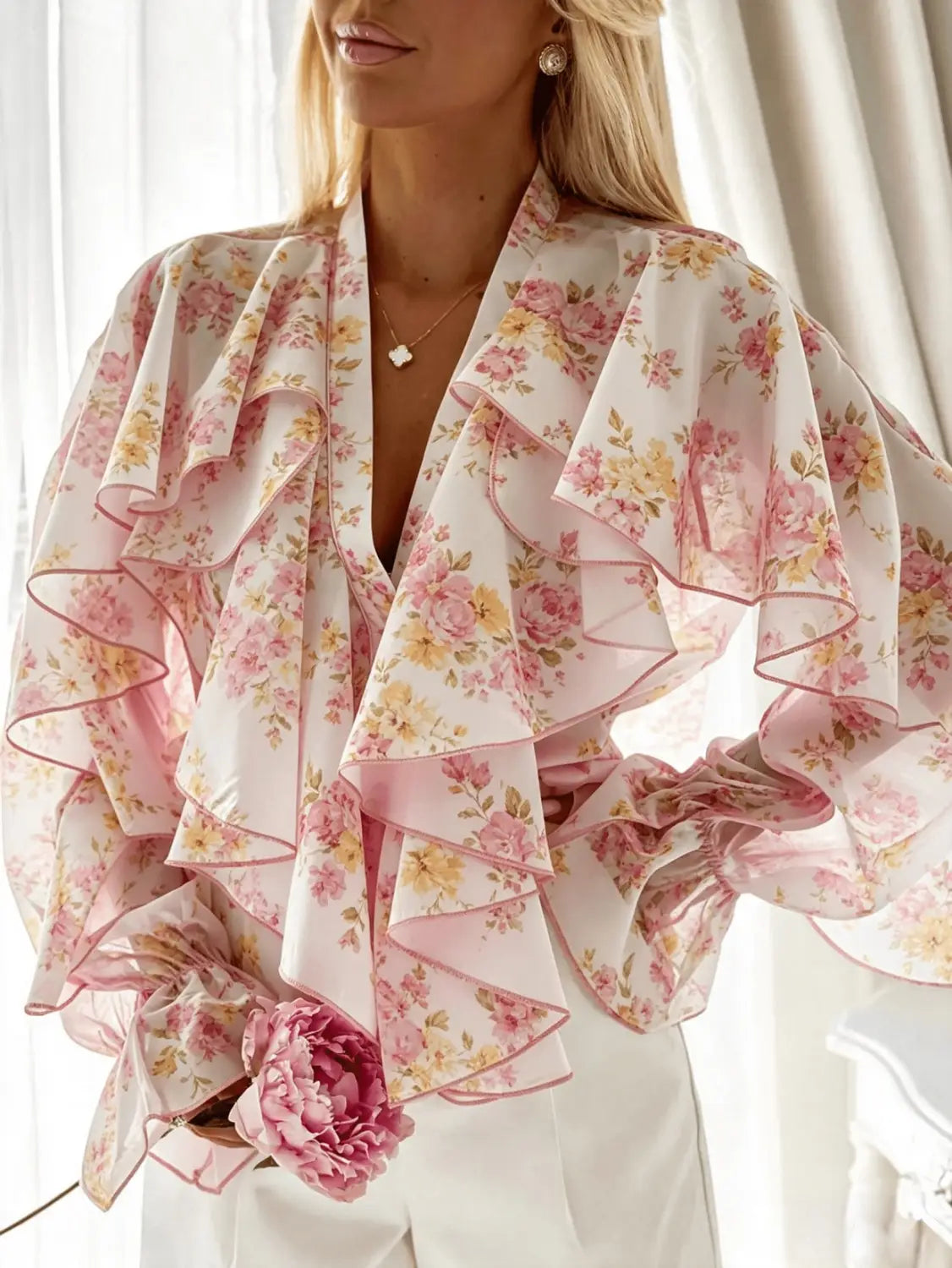 Eine zarte Chiffonbluse mit rosa-weißen Blumenmotiven, langen Ärmeln und mehrlagigen Rüschen, entworfen als lässiges Oberteil.