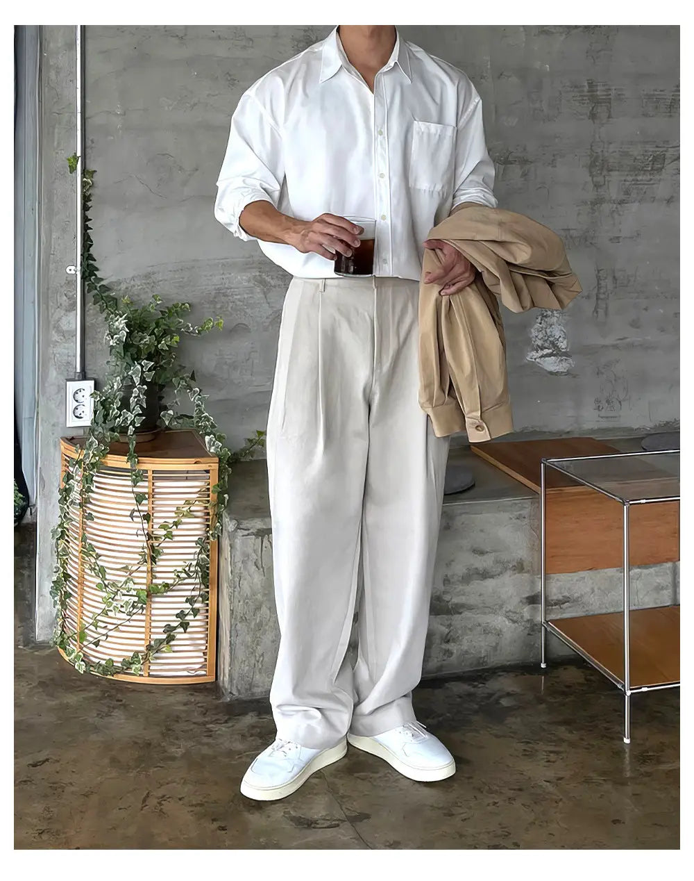Un hombre que viste una camisa blanca abotonada impecable con mangas arremangadas y pantalones de vestir anchos plisados color gris oscuro para hombre.