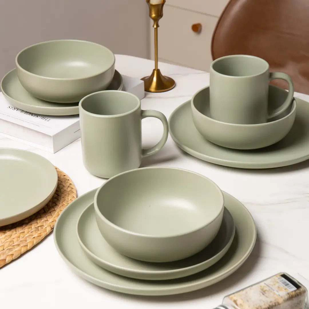 ensemble de vaisselle en grès vert sauge mat, comprenant des bols, des assiettes et des tasses, disposé sur une table à partir de l’ensemble de vaisselle de 12 pièces pour 3.