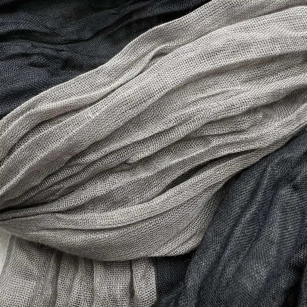 Una bufanda de color gris negro con textura suave y aspecto arrugado, con un tejido sutil tipo malla y pliegues delicados.