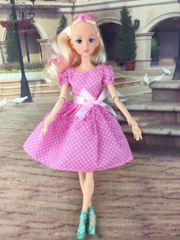 Eine Anziehpuppe mit blondem Haar und blauen Augen in einem pinkfarbenen Fashion-Set mit Punkten mit puffigen Ärmeln und einem passenden Riemen mit Schleife für Kinder.