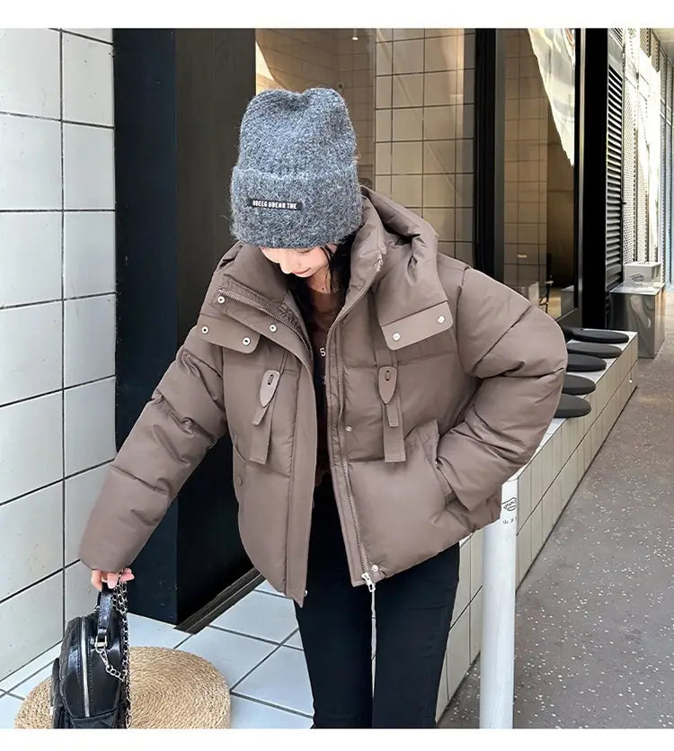 Veste courte matelassée marron à capuche pour femme, fermeture éclair avant sur le devant et plusieurs poches à rabat, avec quincaillerie à tons argentés, conçue pour l’habillement d’hiver chaud