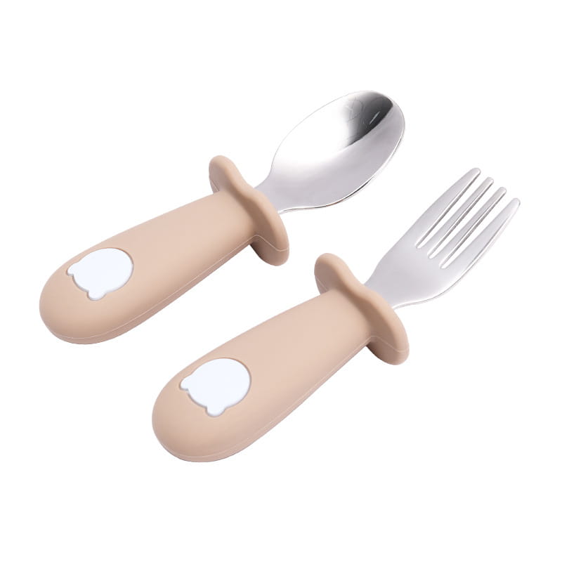Ensemble cuillère et fourchette pour bébé à manches en silicone beige, avec des têtes en acier inoxydable, présentant un motif de tête d’ours blanc, conçu pour les tout-petits.