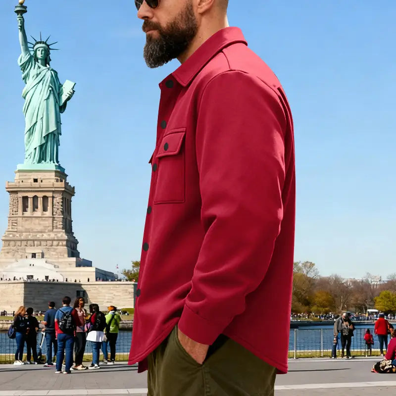 Ein Mann, der eine kräftige rote schwere Fleece-Innenjacke für Herren mit langen Ärmeln, dunklen Knöpfen und Patten an den Taschen trägt.