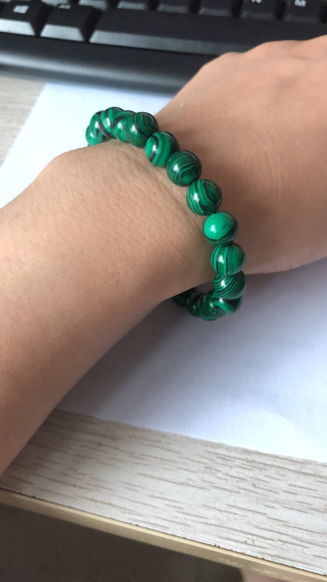 A vibrant green malachite bead bracelet with matte black elastic beads worn on a wrist.
