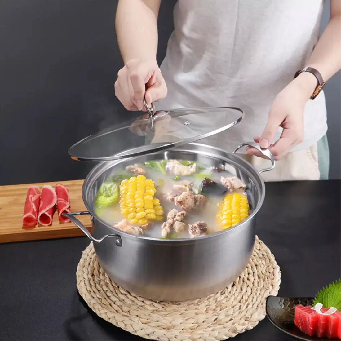 stainless steel induction cookware set 11 pieces featuring a stainless steel pot with clear glass lid and two side handles filled with simmering broth corn vegetables and meat.