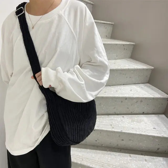 Black corduroy crossbody shoulder bag with an adjustable silver buckle strap for versatile use.