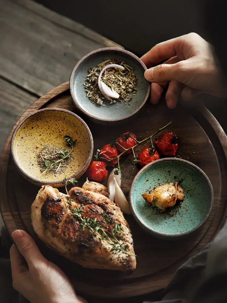 Ceramic sauce dish rustic Japanese dipping bowl displayed with grilled chicken breast seasoned with fresh thyme and herbs served on a wooden platter alongside roasted cherry tomatoes.