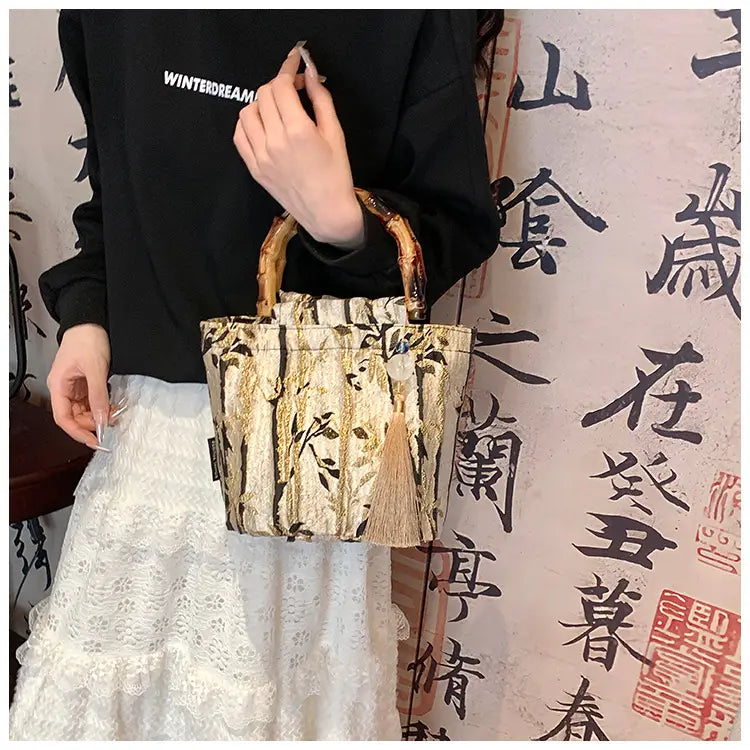 A beige and black patterned fabric bamboo handbag with tassel and bamboo handle accents.