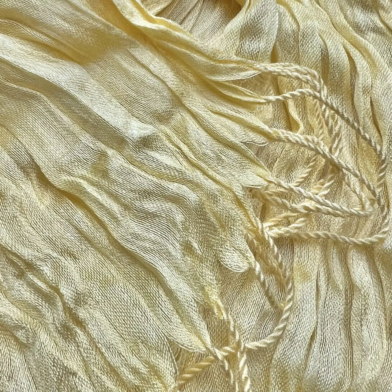 Un foulard froissé jaune pâle délicat, fabriqué dans une soie d’été texturée, avec une brillance subtile et des plis souples.