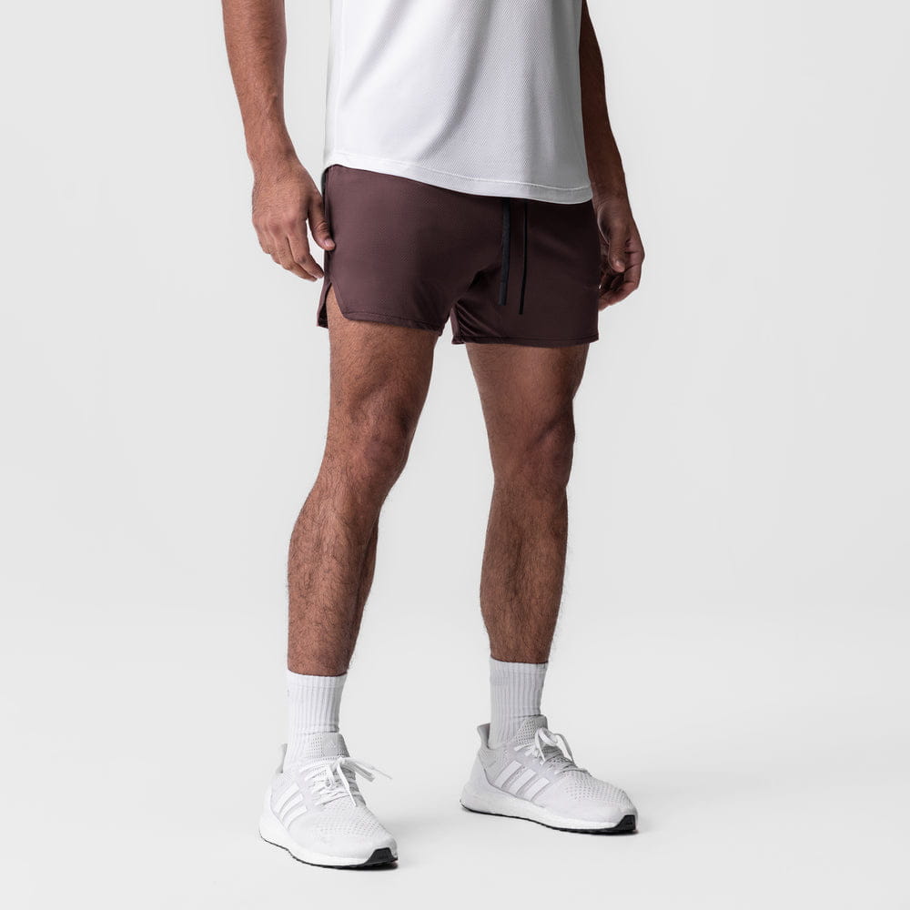 men quick dry athletic sports shorts in brown featuring a drawstring waist and side pockets worn by a model in a minimalist studio setting