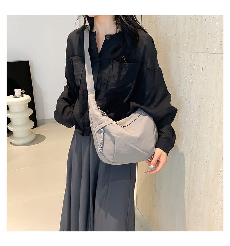 Light gray nylon crossbody bag with subtle textured strap and zipper closure designed as a large capacity hobo shoulder bag.