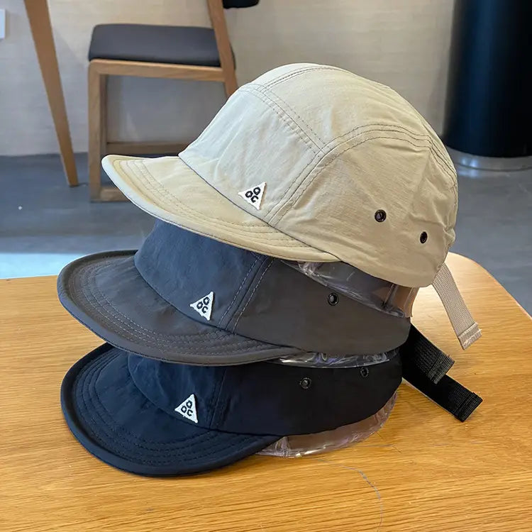Stacked beige gray and black quick drying five panel caps with white triangular logos on the front for outdoor use.
