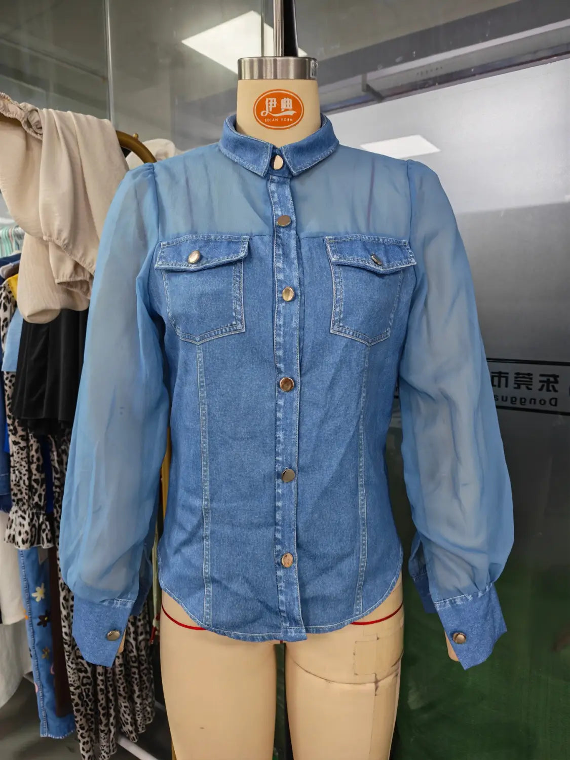 Chemise boutonnée en denim bleu clair à manches longues et deux poches poitrine, présentée dans un haut à encolure en V à manches transparentes en denim.