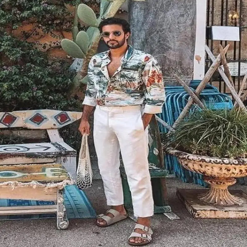Ein Mann, der weiße Herren-Cotton-Linen-Freizeit-Hosen mit hohem Stretchanteil trägt, kombiniert mit einem lebhaften Button-up-Hemd mit tropischem Print und umgekrempelten Ärmeln.