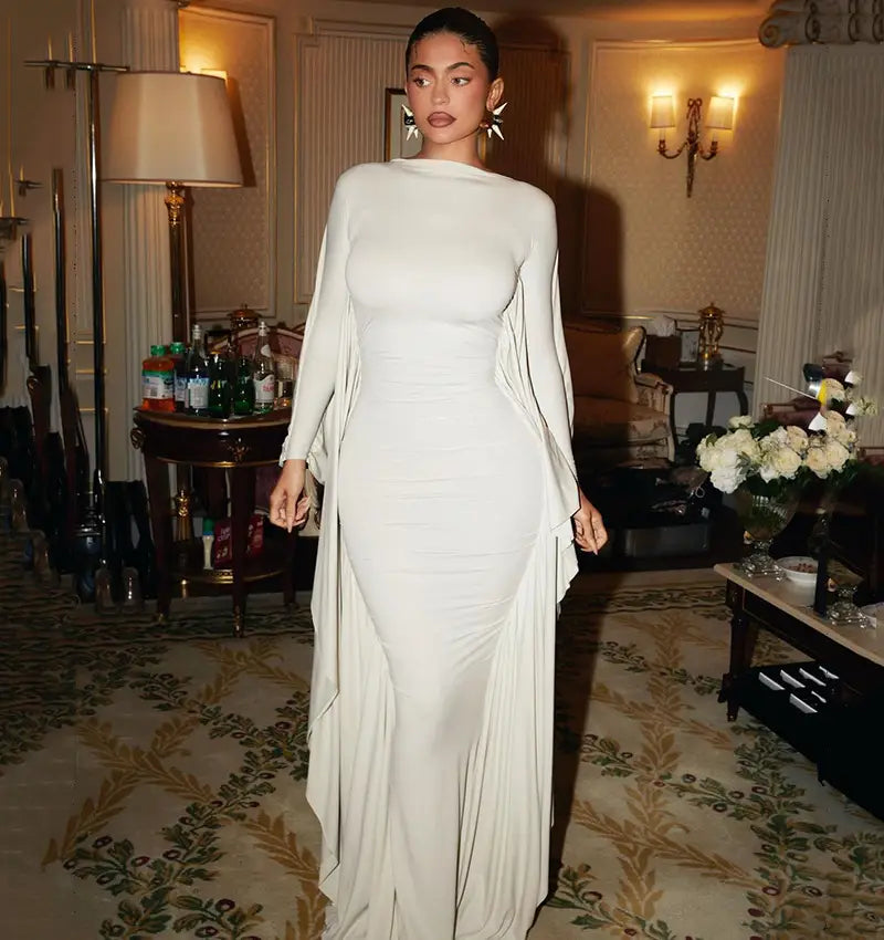 A sleek off-white asymmetrical satin batwing sleeve maxi dress with long sleeves and a flowing cape-like overlay.