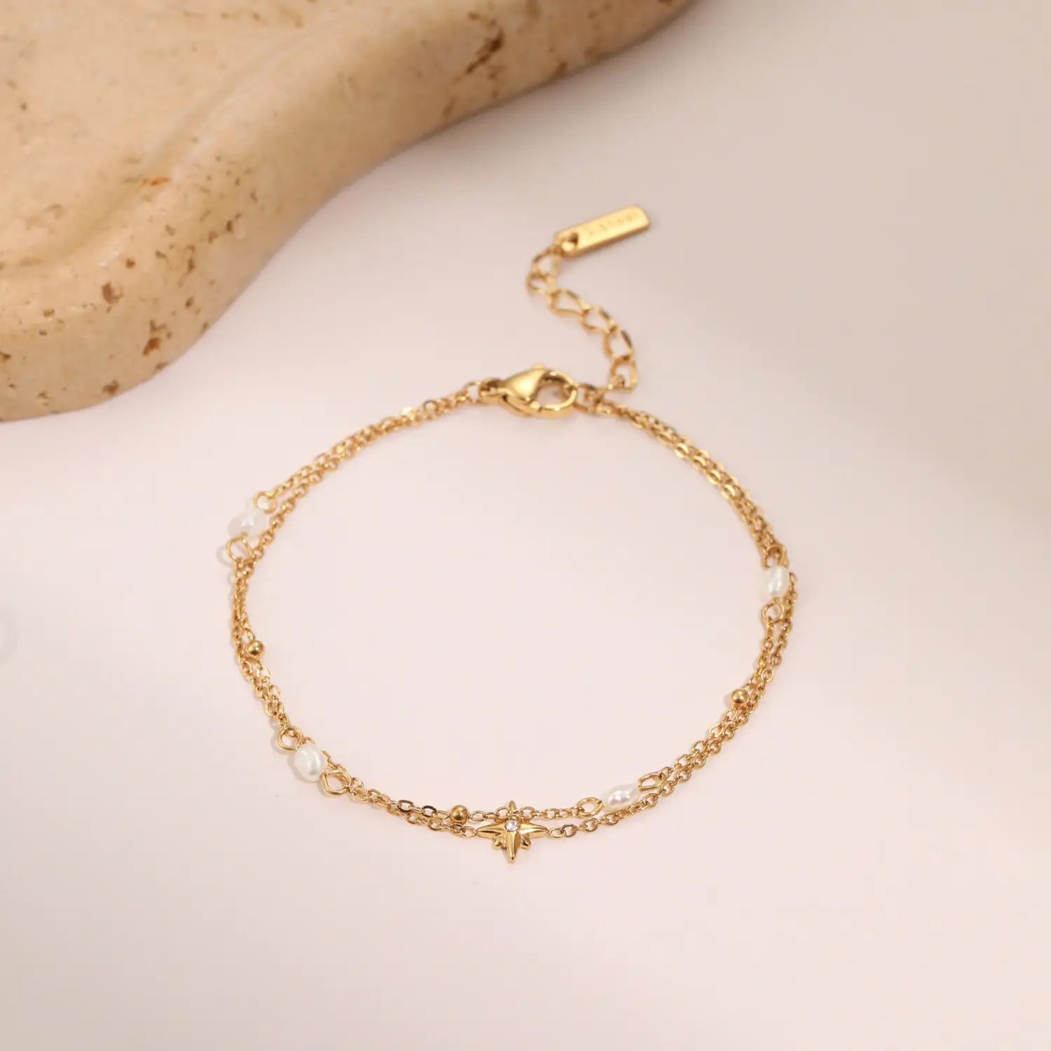 Gold-toned double-layer chain bracelet made of stainless steel adorned with small white pearls and a central star-shaped charm.