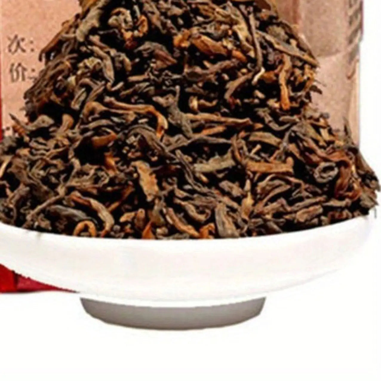 Eine weiße Keramikschale, die einen Büschel dunkelbraunem, verwundenem und eingerolltem losem Premium-Yunnan-Reif-Puer-Tee für den Gesundheitsvorsorge-Teekuchen mit 500 g enthält.