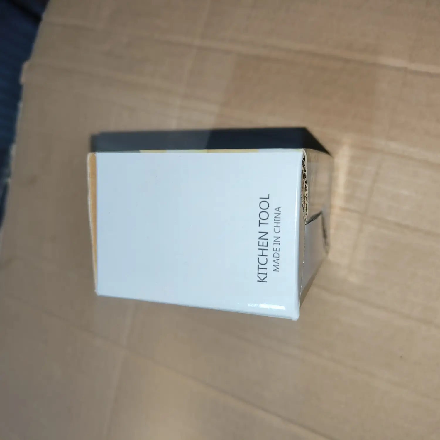 Boîte en carton blanc étiquetée comme ustensile de cuisine avec texte noir et panneau latéral gris foncé contenant un outil de hachage-presse-ail manuel ergonomique en acier inoxydable.