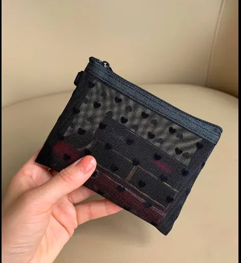Ein schwarzes Mesh-Geldbörschen mit Reißverschluss und dezenten roten Akzenten mit einem schwarzen Herz-Punkte-Muster, das als Mesh-Kosmetiktasche verwendet wird.