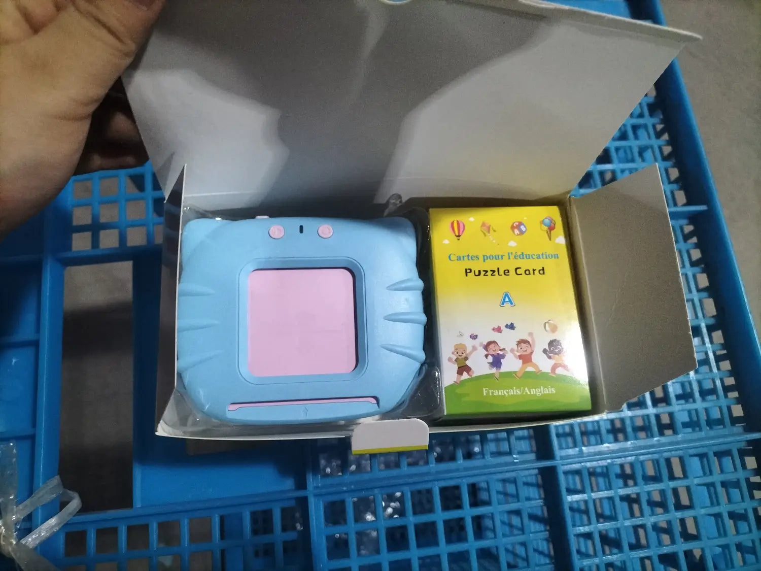 ピンクの画面と上部にある小さなボタン2つを備えた、水色のプラスチック製ハンディ型キッズ用お話カード型の早期学習タブレット。