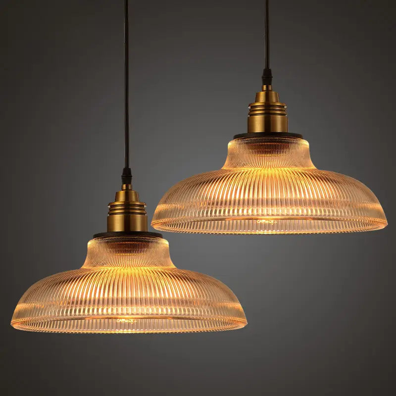 Two warm-toned ribbed glass pendant lights with brass metal fixtures for elegant interior lighting.