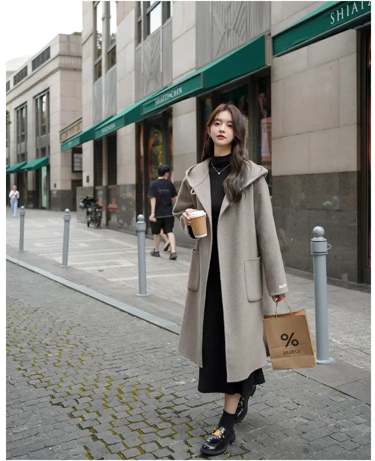 Ein langes beigefarbenes Woll-Longjacke mit Kapuze und vorderen Taschen, geeignet für Winter-Outdoorbekleidung mittlerer Länge.