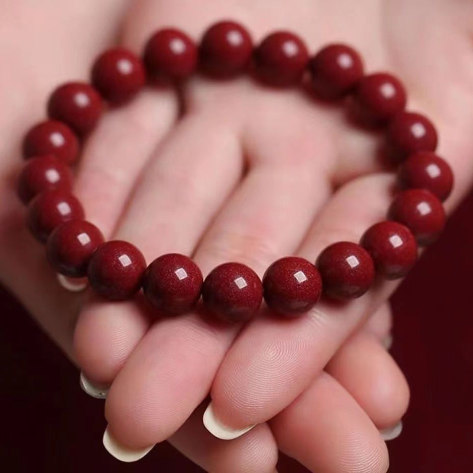 A polished red cinnabar spherical bead bracelet with a smooth deep red finish held in a hand.