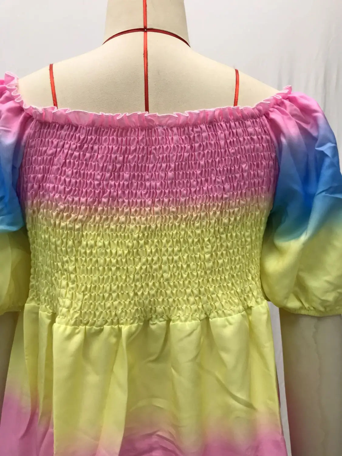 A vibrant rainbow gradient off-the-shoulder top with smocked texture and puffy sleeves shown alongside a floral print smocked tiered midi dress with square neckline.