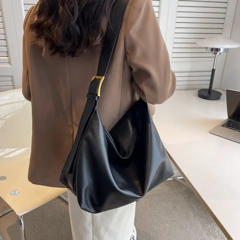 Black faux leather shoulder bag with gold-tone buckle and adjustable strap suitable for daily use.