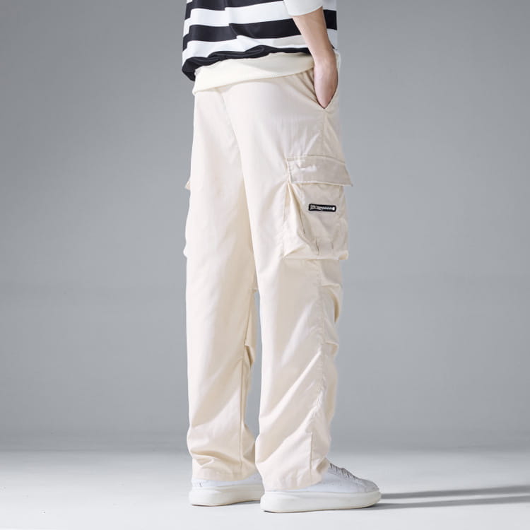 Beige mens multi pocket cargo workwear pants featuring multiple pockets and a small black brand patch on the thigh.