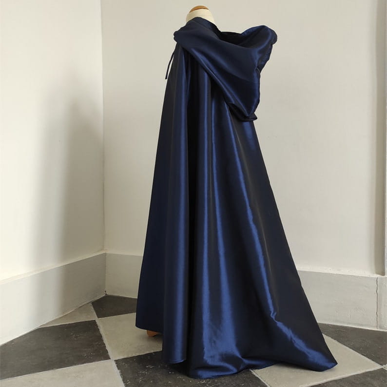 A deep navy satin cape with a hood draped elegantly over a mannequin in front of a wooden cat tree scratching post and condo.