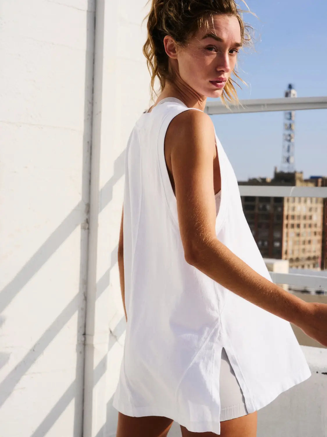 A back view of a white sleeveless cotton wrap vest top with a relaxed v neck fit and a back slit.