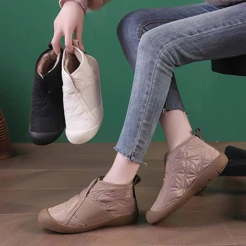 Cream-colored waterproof plush winter snow ankle boot with quilted design, brown rubber sole, and elastic side panel.