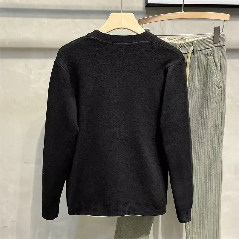 Herren-Strickcardigan in schwarzem Strick mit gerippten Bündchen und Saum, präsentiert auf einem hölzernen Kleiderbügel.