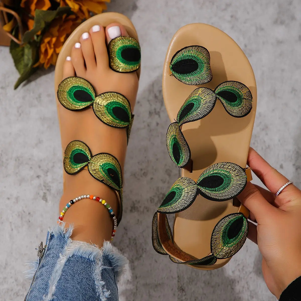 Beige flat sandals for women embellished with peacock feathers featuring green and gold embroidery.