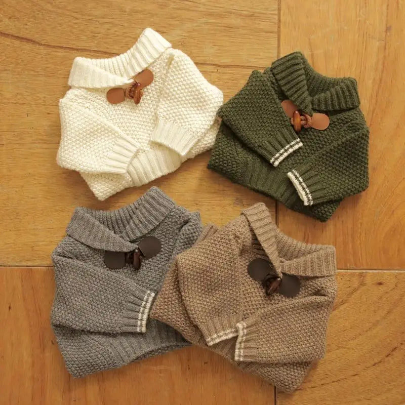 four knitted dog sweaters in cream olive green gray and beige with ribbed collars featuring white trim and decorative button closures for pet winter apparel