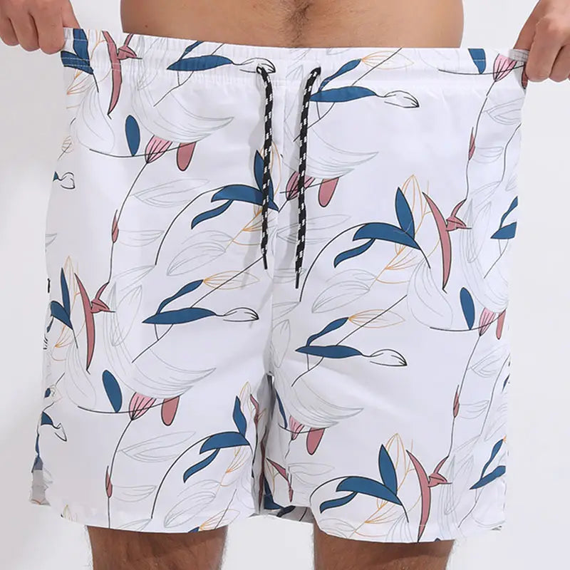 Men printed swim trunks featuring a vibrant botanical print with blue pink and gold leaf motifs on white fabric suitable for sports and beach use.